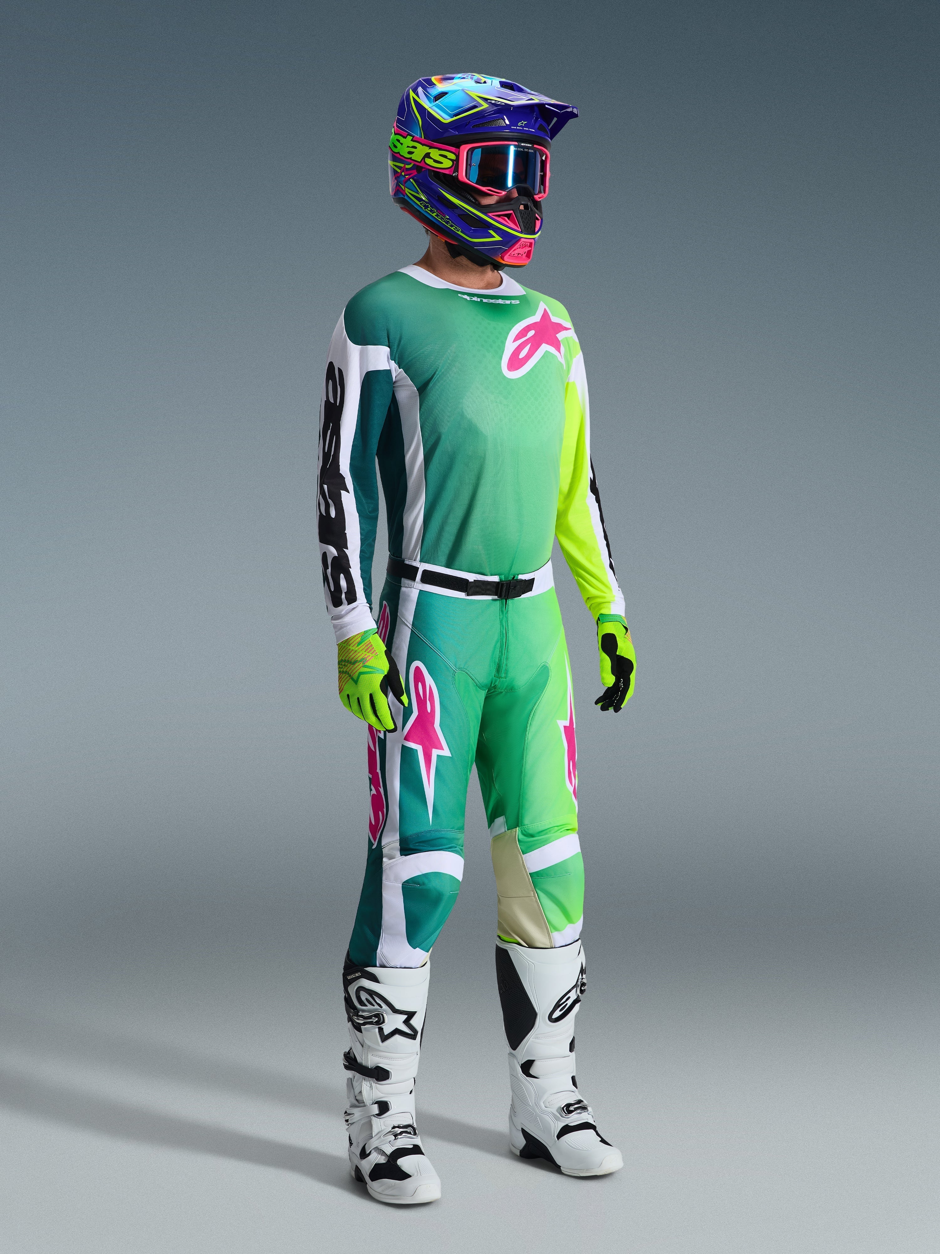Pilota di motocross con attrezzatura completa, maglia Racer Portl 2026 verde con maniche bianche e nere e logo rosa, pantaloni verdi coordinati con accenti rosa, casco multicolore con maschera, stivali bianchi e neri e guanti verdi, completo coordinato per il fuoristrada