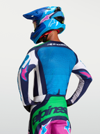 Alpinestars Maglia Techstar Maven, maglia da motocross blu e verde con accenti rosa, vista posteriore su modello con casco, abbigliamento racing off-road traspirante