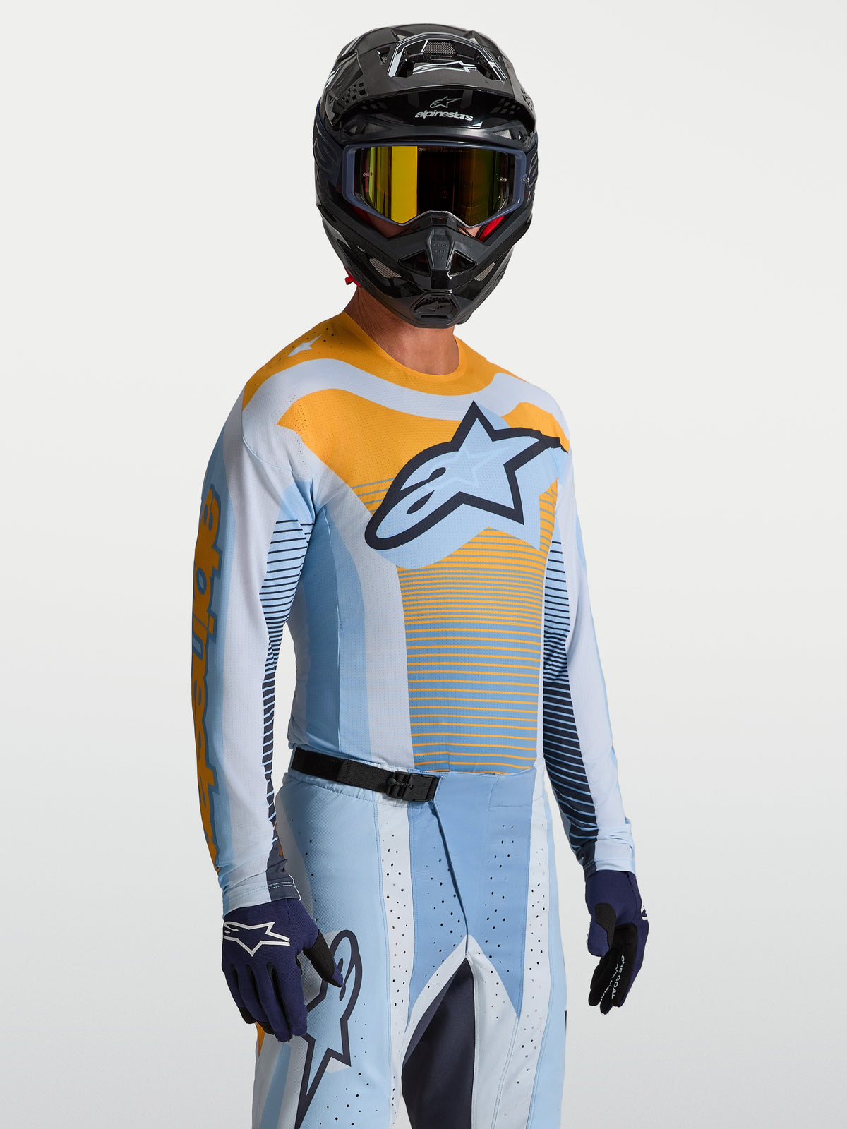 Alpinestars Maglia Techstar Maven, maglia da motocross da uomo, blu e arancione, vestibilità atletica da gara, indossata con casco e guanti coordinati.