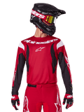 Maglia Alpinestars 2025 Fluid Haul, maglia da motocross, rosso acceso e nero, indossata come parte di un set completo con pantaloni e guanti coordinati, casco nero con occhiali a lente gialla, branding e loghi bianchi, abbigliamento da corsa fuoristrada ad alte prestazioni.