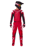 Alpinestars 2025 Fluid Haul Gear Set, completo da motocross in rosso acceso e nero, caratterizzato da una maglia rossa con maniche nere e branding bianco, pantaloni rossi coordinati con loghi a stella bianchi, casco nero con occhiali dalle lenti dorate e stivali rossi, equipaggiamento completo per fuoristrada