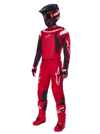 Pilota di motocross che indossa il set Alpinestars 2025 Fluid Haul, rosso brillante con accenti neri e bianchi, completo di maglia, pantaloni, casco, stivali e guanti, progettato per prestazioni e protezione fuoristrada