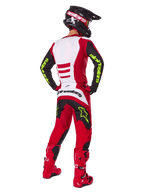 Pilota di motocross visto da dietro con set completo Alpinestars Fluid Haul 2025, rosso brillante e nero con pannelli bianchi, logo giallo neon su maniche e pantaloni, stivali rossi e casco nero, equipaggiamento professionale per fuoristrada