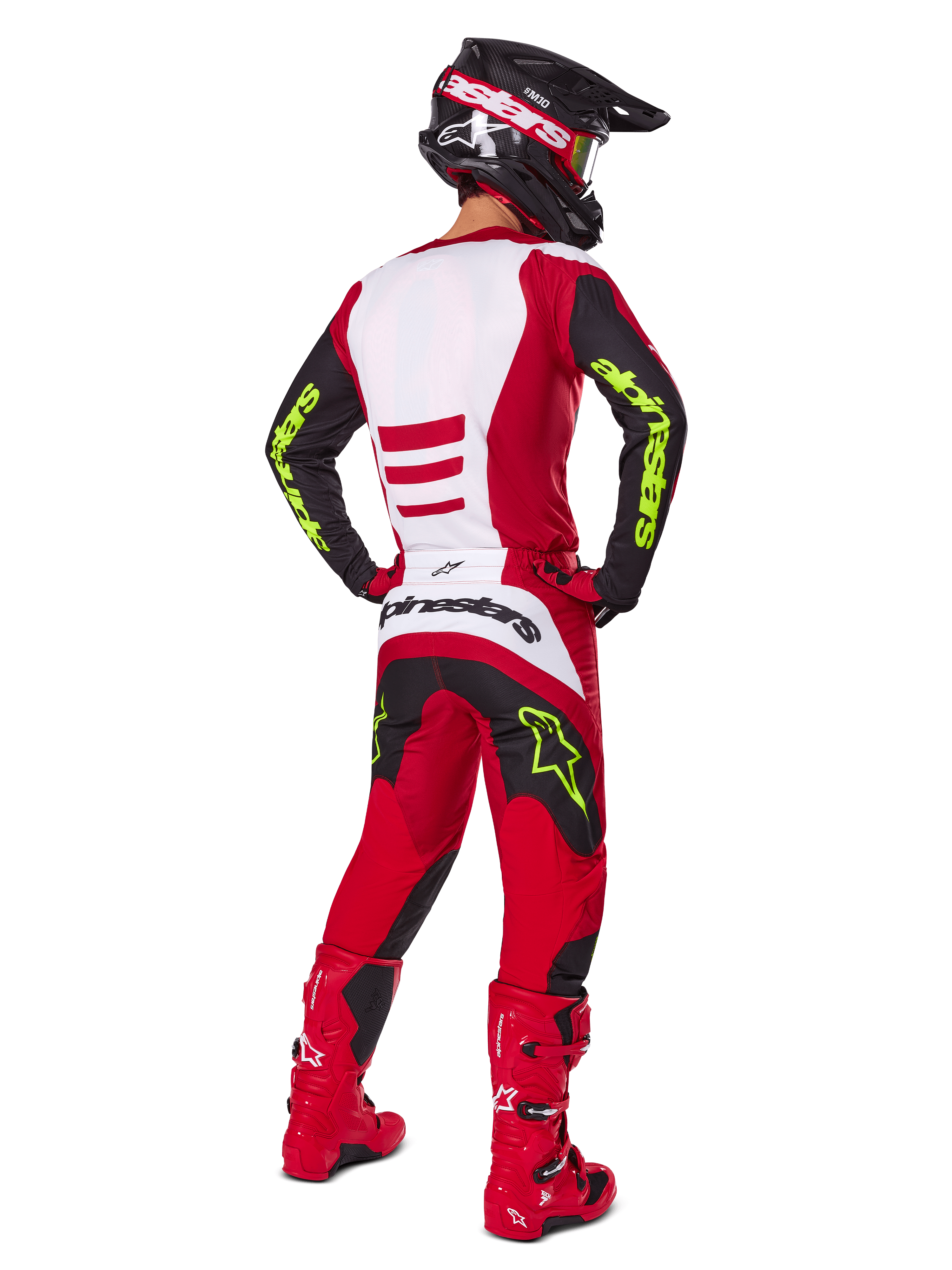 Pilota di motocross visto da dietro con set completo Alpinestars Fluid Haul 2025, rosso brillante e nero con pannelli bianchi, logo giallo neon su maniche e pantaloni, stivali rossi e casco nero, equipaggiamento professionale per fuoristrada