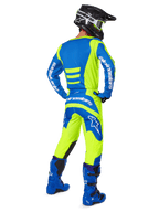 Pilota di motocross visto da dietro che indossa il completo Alpinestars Fluid Haul 2025 in Giallo Fluo e Blu, composto da una maglia blu con dettagli gialli, pantaloni gialli con inserti blu su seduta e ginocchia, abbinati a stivali blu acceso e casco nero.