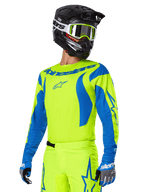Alpinestars 2025 Fluid Haul Gear Set, maglia e pantaloni da motocross, giallo brillante e blu, indossato con casco nero e occhiali con montatura gialla, caratterizzato da motivi blu a onda sulle maniche e loghi a stella blu sui pantaloni, completo da gara fuoristrada coordinato