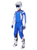 Pilota di motocross che indossa il set completo 2025 Fluid Haul, maglia e pantaloni blu e bianchi con logo Alpinestars, casco bianco con occhiali blu, stivali bianchi e guanti blu, completo da gara coordinato per motocross fuoristrada.
