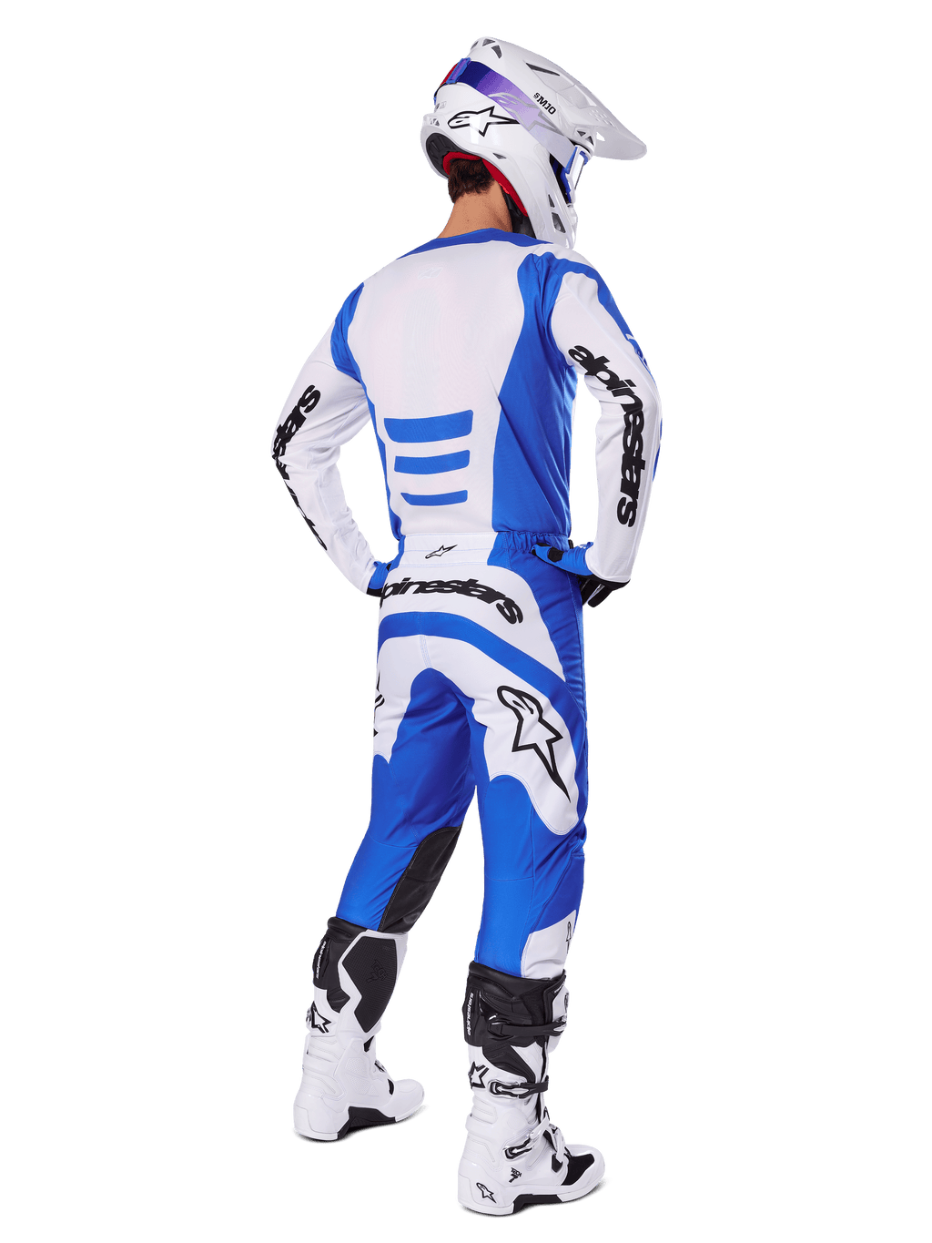 Pilota di motocross di spalle con completo Alpinestars 2025 Fluid Haul, maglia blu e bianca con pantaloni coordinati, casco bianco con dettagli blu e stivali da corsa bianchi e neri, abbigliamento da gara fuoristrada coordinato