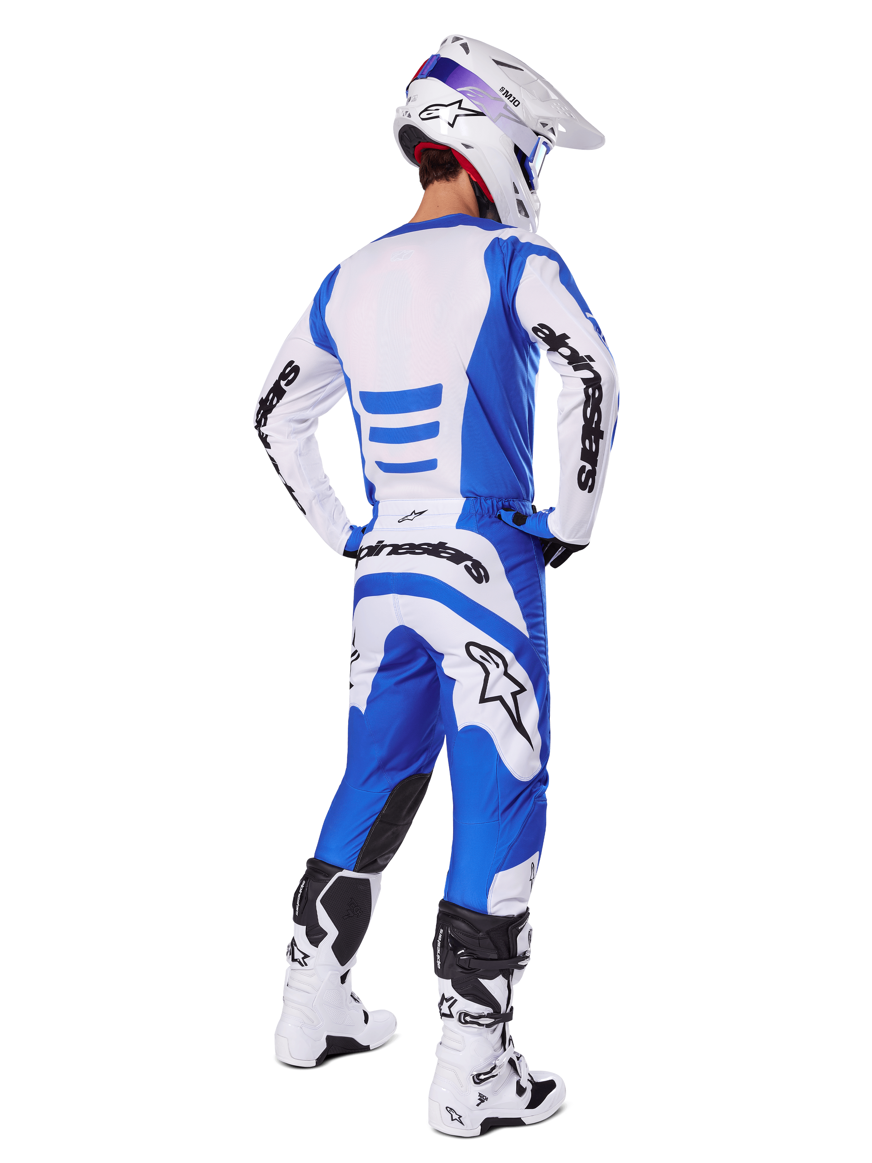 Pilota di motocross di spalle con completo Alpinestars 2025 Fluid Haul, maglia blu e bianca con pantaloni coordinati, casco bianco con dettagli blu e stivali da corsa bianchi e neri, abbigliamento da gara fuoristrada coordinato