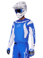 Pilota di motocross che indossa il set di abbigliamento Alpinestars 2025 Fluid Haul in blu e bianco, con maglia blu e accenti bianchi, pantaloni blu coordinati con loghi a stella, casco bianco con occhiali blu e guanti coordinati blu e grigi, outfit completo da gara off-road.