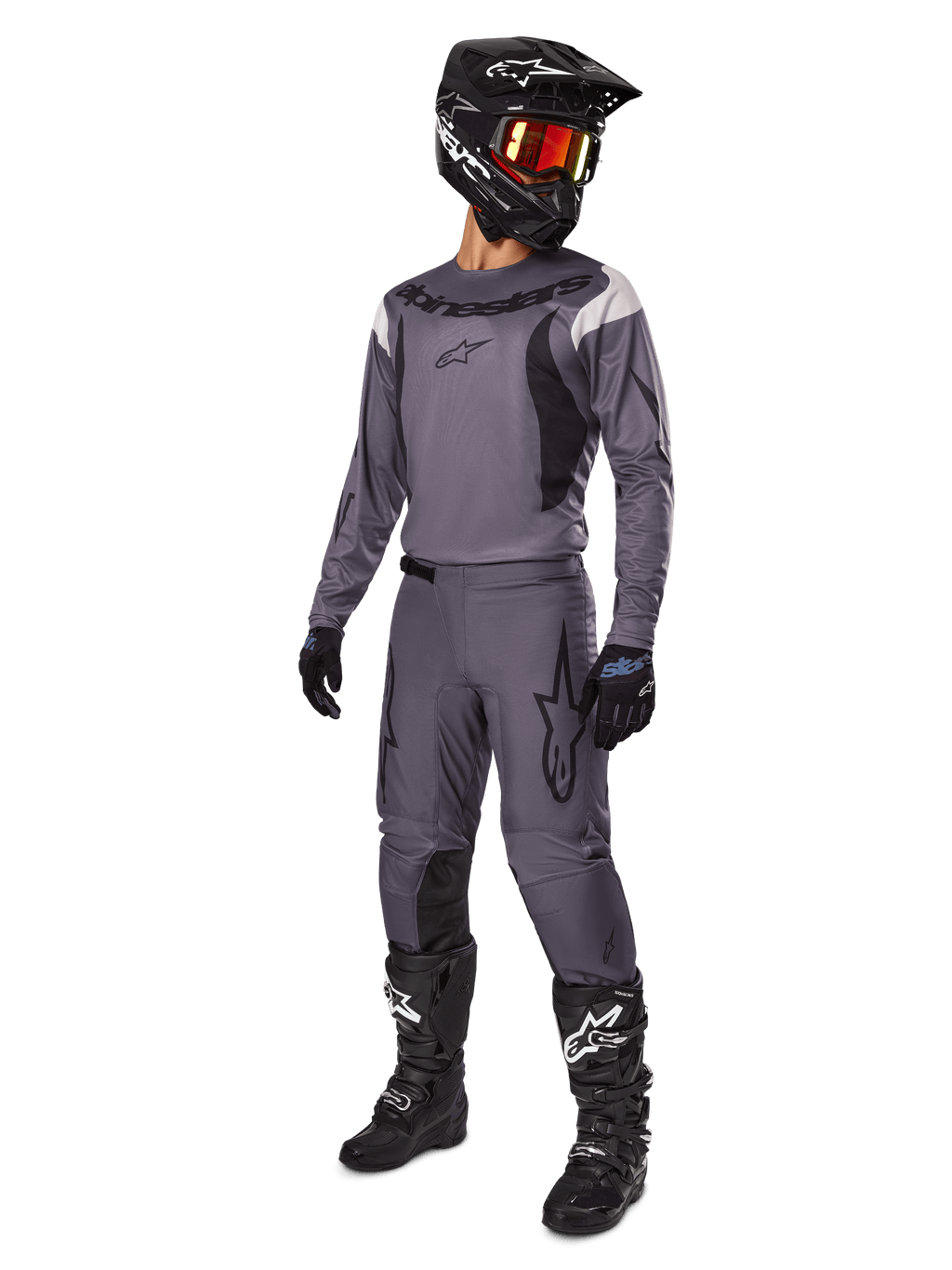 Pilota di motocross con set Alpinestars Fluid Haul 2025 grigio, maglia e pantaloni grigi con dettagli neri, casco nero con occhiali rossastri, guanti neri e stivali neri con loghi bianchi, completo da gara off-road