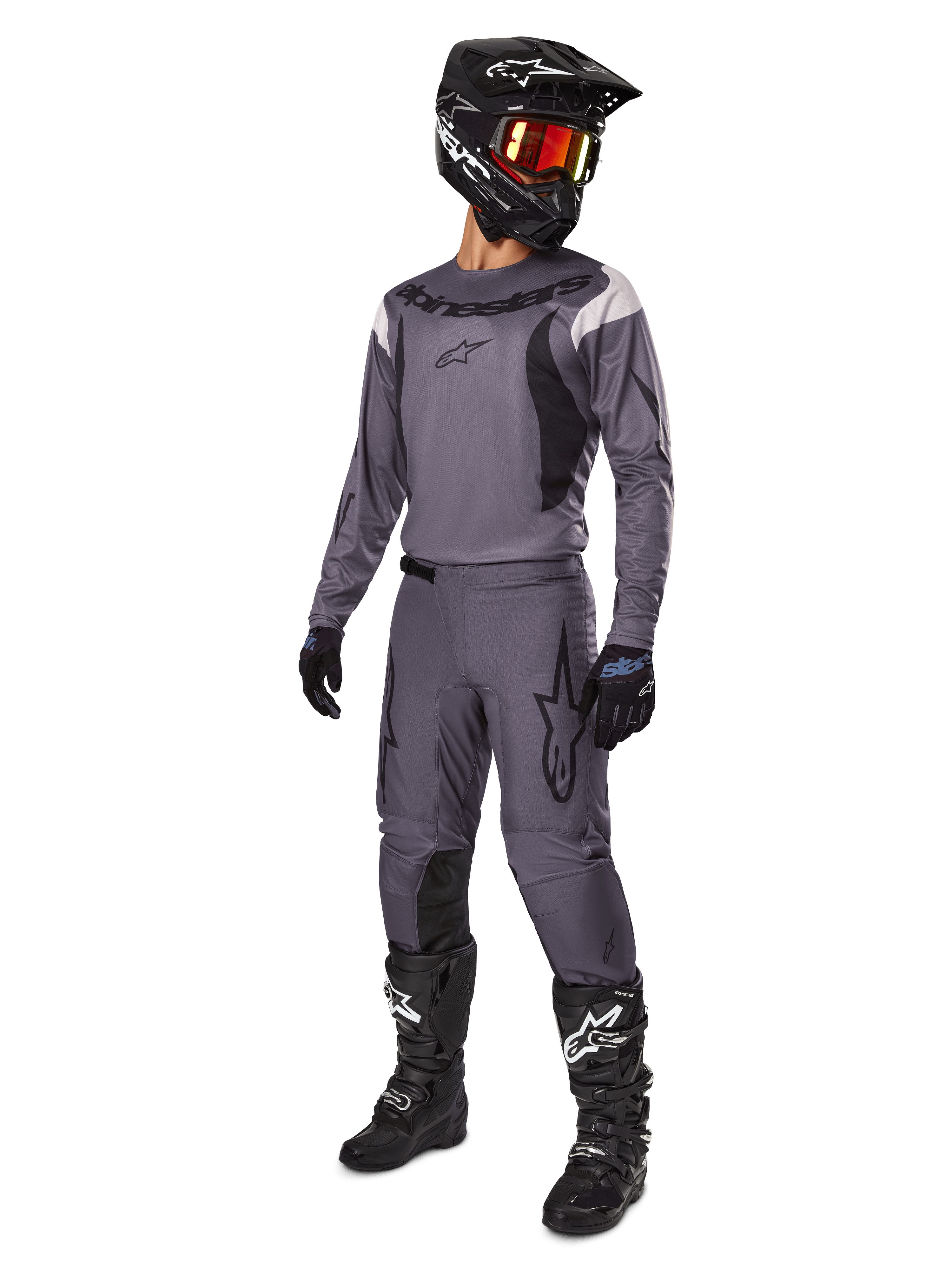 Pilota di motocross con set Alpinestars Fluid Haul 2025 grigio, maglia e pantaloni grigi con dettagli neri, casco nero con occhiali rossastri, guanti neri e stivali neri con loghi bianchi, completo da gara off-road