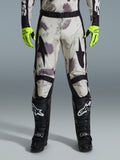 Alpinestars 2026 Racer Lahnd Pants, pantaloni da motocross, motivo Sand Camo con grafiche astratte grigie e viola, indossati con guanti giallo neon e stivali neri, con loghi a stella neri sulle cosce e cintura nera in vita, abbigliamento da gara off-road resistente
