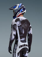 Completo Alpinestars Racer Lahnd 2026, pilota di motocross visto da dietro con maglia e pantaloni con grafica punteggiata bianco e nero, casco Alpinestars blu e bianco e guanti neri, abbigliamento tecnico per corse fuoristrada