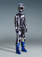 Alpinestars 2026 Racer Lahnd Gear Set, pilota di motocross con maglia e pantaloni a fantasia bianca e nera dal design astratto effetto invecchiato, grande logo Alpinestars bianco, stivali blu e viola vivaci e casco bianco e blu, outfit professionale completo per corse off-road.