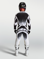 Alpinestars Maglia e Completo Techstar Swan, completo motocross da uomo, bianco e nero con grafiche splatter posteriori, vista posteriore su un pilota, abbigliamento off-road