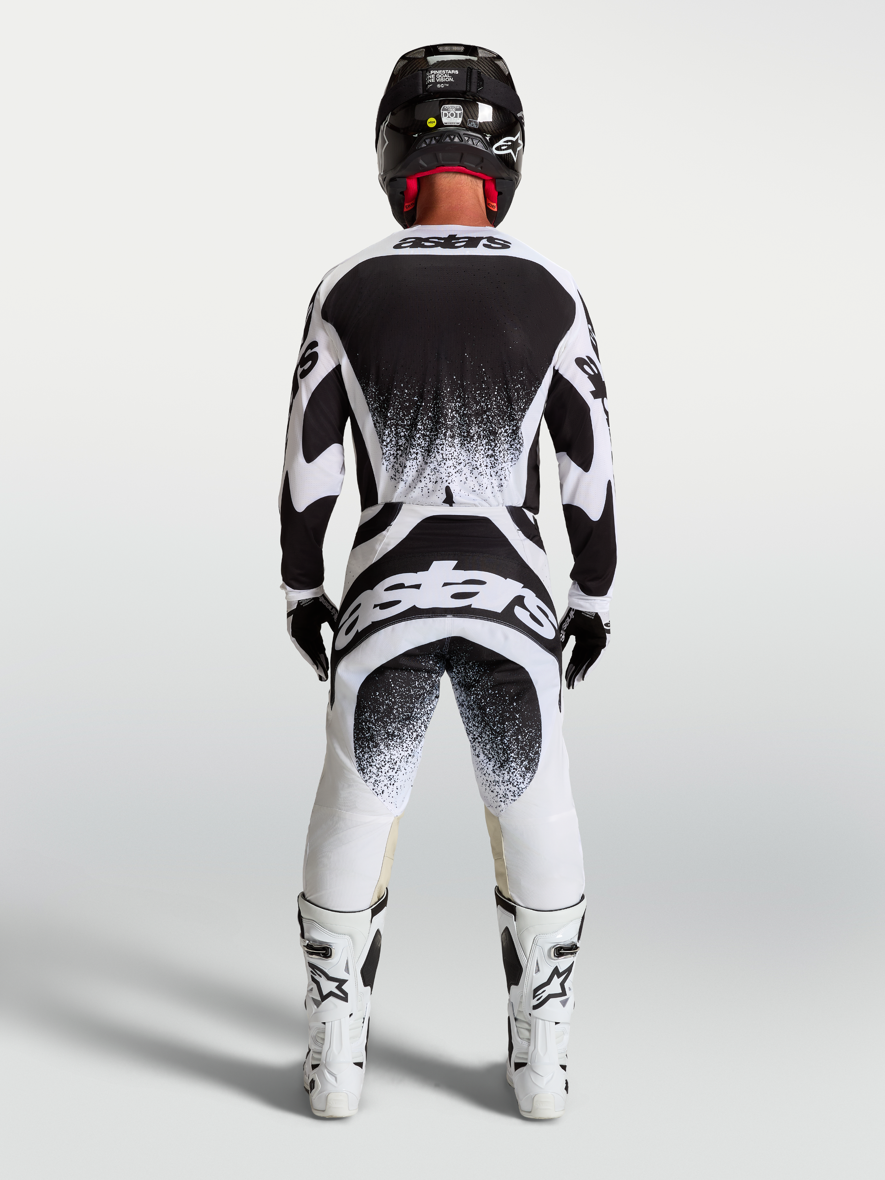 Alpinestars Maglia e Completo Techstar Swan, completo motocross da uomo, bianco e nero con grafiche splatter posteriori, vista posteriore su un pilota, abbigliamento off-road