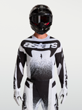 Alpinestars Maglia Techstar Swan, maglia da motocross da uomo, bianco e nero, tessuto elasticizzato leggero con perforazioni laser per la ventilazione, vestibilità atletica racing, indossata da un pilota con casco e guanti coordinati