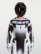 Alpinestars Maglia Techstar Swan, maglia da motocross da uomo, bianco e nero, tessuto elasticizzato leggero con perforazioni laser per la ventilazione, vestibilità atletica racing, indossata da un pilota con casco e guanti coordinati