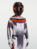 Alpinestars Maglia Techstar Swan, maglia da motocross uomo grigia e rosso fluo, vestibilità racing, indossata con casco.