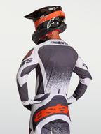 Alpinestars Maglia Techstar Swan, maglia motocross atletica da uomo, grigio scuro e bianco con dettagli rossi, vista posteriore su pilota con casco, tessuto traspirante e ventilato