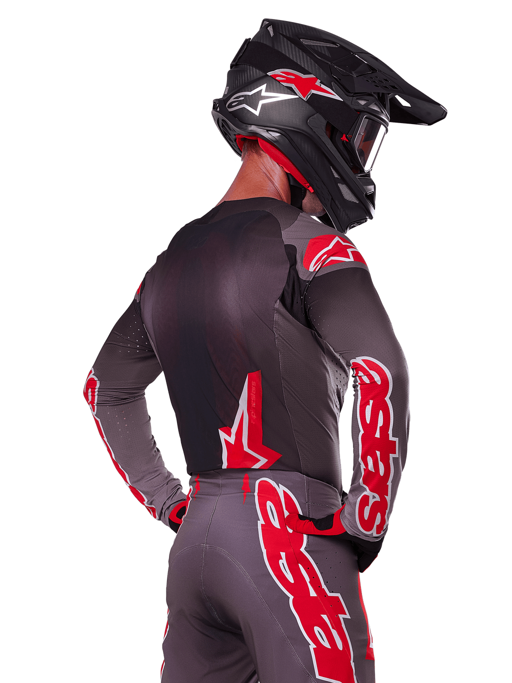 Alpinestars 2025 Supertech Lipan Gear Set, pilota di motocross visto di spalle, maglia e pantaloni grigio antracite con vivace marchio 'astars' rosso sulle maniche e sulla schiena, abbinato a un casco nero