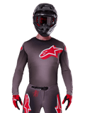 Alpinestars Supertech Lipan Jersey 2025, maglia da motocross, color fumo e rosso, con un grande logo rosso e bianco sul petto, indossata con casco nero e guanti rossi e neri, vestibilità atletica da gara con perforazioni laser