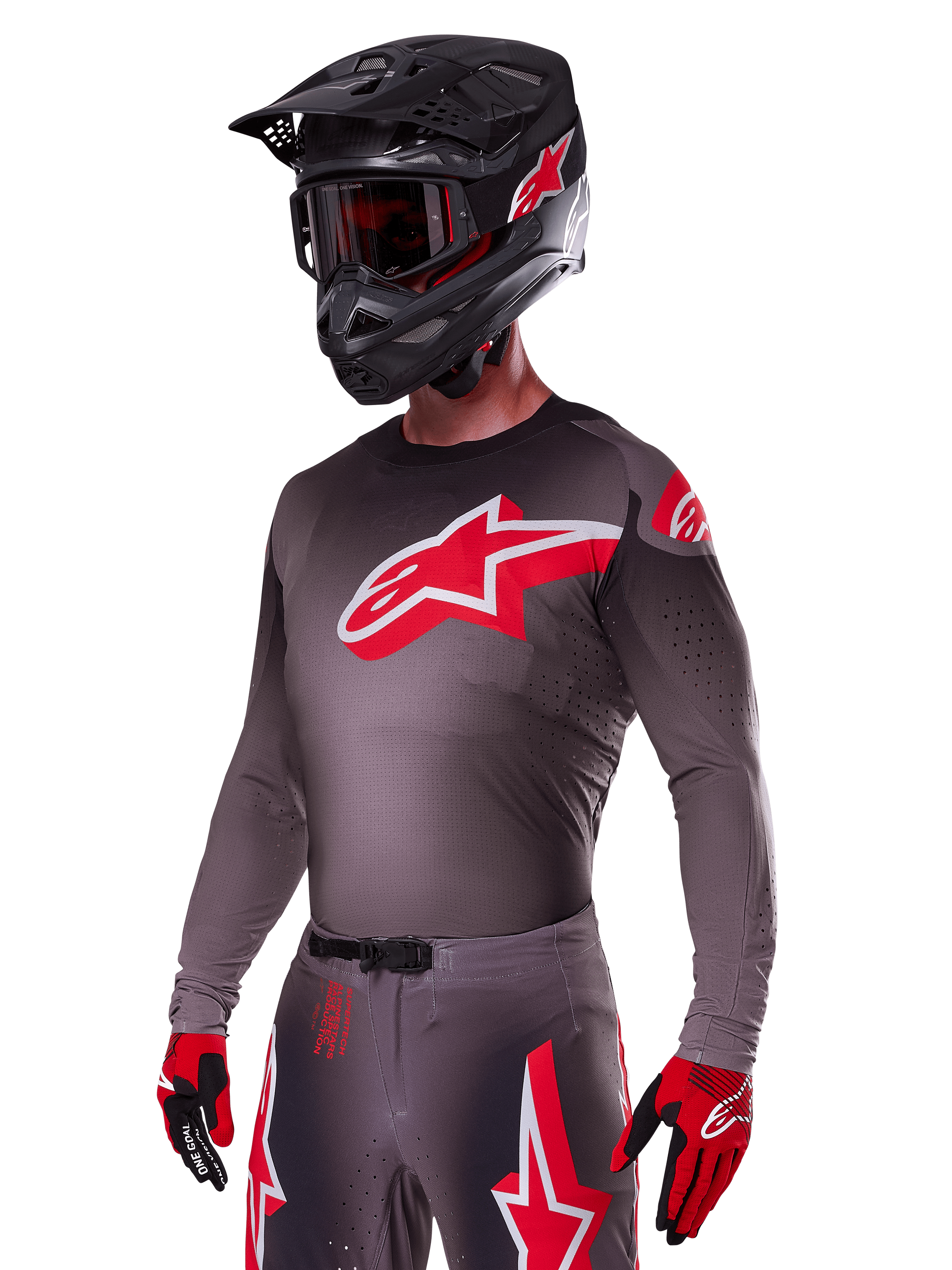 Set Alpinestars 2025 Supertech Lipan, pilota di motocross che indossa maglia e pantaloni grigio scuro con accenti rossi e bianchi, con un grande logo Alpinestars rosso sul petto, perforazioni al laser per la ventilazione, casco nero coordinato, maschera rossa e guanti rossi e neri.