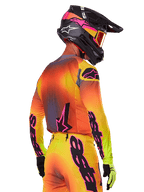Pilota di motocross visto da una prospettiva posteriore-laterale con il set Alpinestars 2025 Supertech Lipan, caratterizzato da un gradiente giallo, arancione e rosso con branding nero e rosa, casco nero con accenti rosa e maschera arancione, abbigliamento professionale per gare off-road.