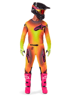 Pilota di motocross con abbigliamento da gara completo, maglia e pantaloni Supertech Lipan 2025 in una sfumatura gialla e arancione con accenti rosa, casco nero con grafiche rosa coordinate, stivali rosa acceso e guanti verde lime, completo da corsa off-road Alpinestars coordinato.