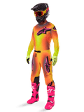 Pilota di motocross che indossa il completo Alpinestars Supertech Lipan 2025, maglia e pantaloni con sfumatura giallo e arancione e accenti rosa, casco nero con maschera giallo-rossa, guanti giallo acceso e stivali rosa vivace, abbigliamento da gara off-road coordinato