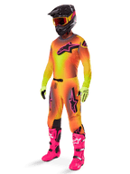 Pilota di motocross che indossa il completo Alpinestars Supertech Lipan 2025, maglia e pantaloni con sfumatura giallo e arancione e accenti rosa, casco nero con maschera giallo-rossa, guanti giallo acceso e stivali rosa vivace, abbigliamento da gara off-road coordinato