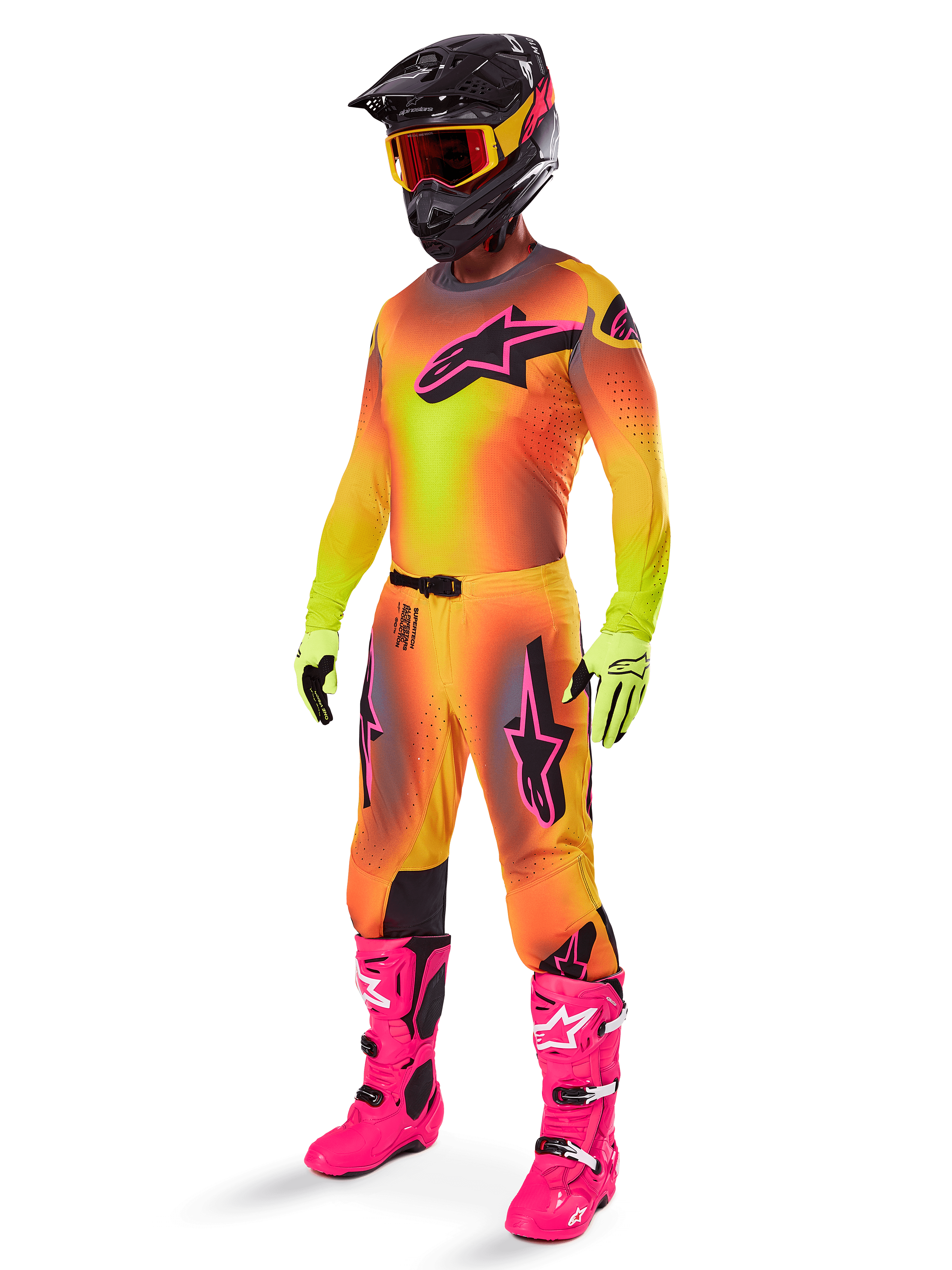 Pilota di motocross che indossa il completo Alpinestars Supertech Lipan 2025, maglia e pantaloni con sfumatura giallo e arancione e accenti rosa, casco nero con maschera giallo-rossa, guanti giallo acceso e stivali rosa vivace, abbigliamento da gara off-road coordinato