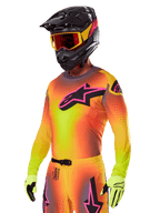 Pilota di motocross con Set Gear Alpinestars Supertech Lipan 2025, maglia con sfumatura gialla e arancione e logo Astars rosa e nero, guanti giallo neon, casco nero con occhiali rossi, abbigliamento professionale da gara fuoristrada