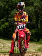 Pilota di motocross seduto su una moto da cross Honda rossa con il numero di gara 18, che indossa la maglia Alpinestars Supertech Lipan 2025 e i pantaloni coordinati in giallo e rosa, stivali Alpinestars rosa acceso, casco Red Bull, abbigliamento professionale da gara per prestazioni fuoristrada.