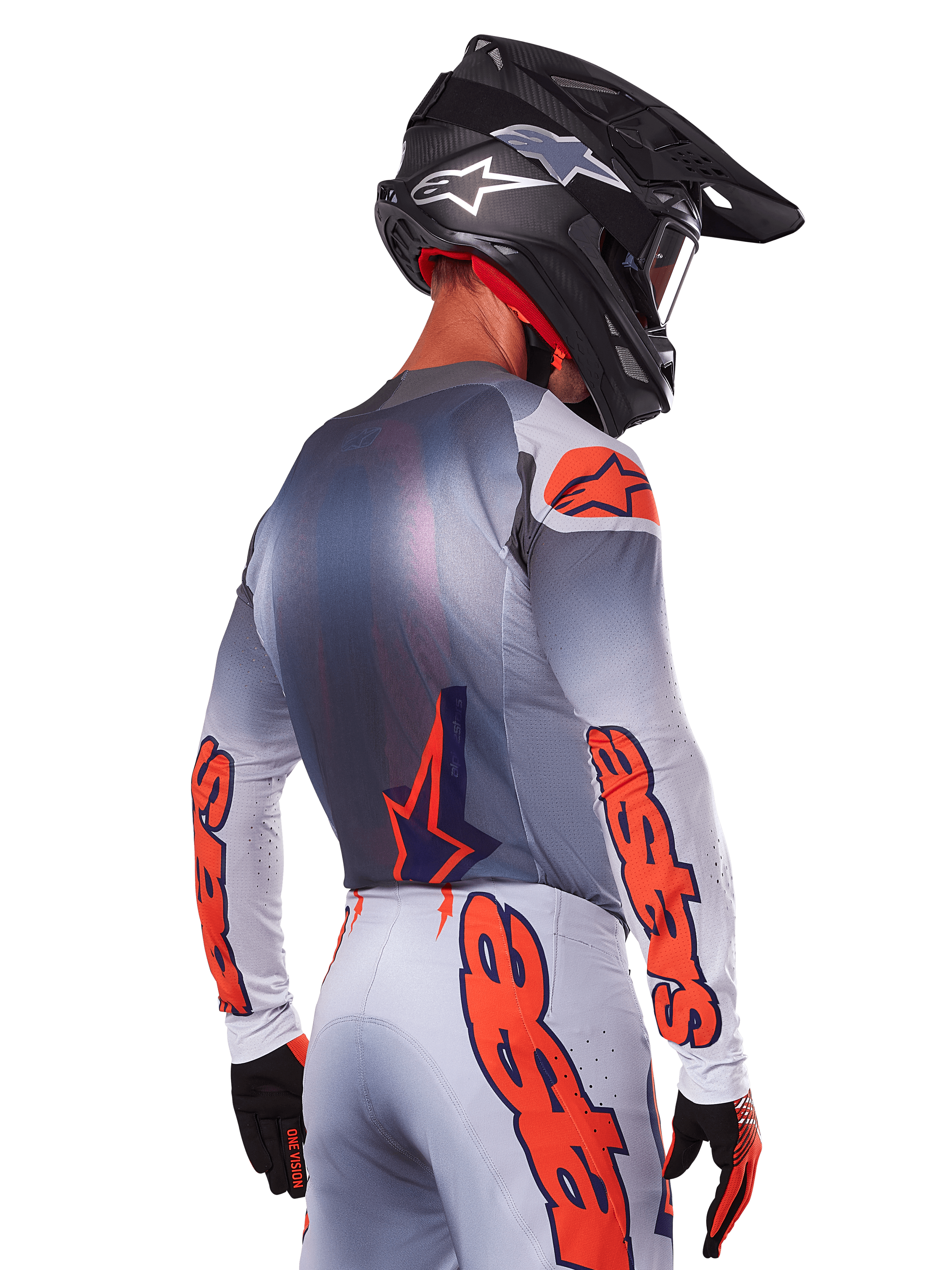 Pilota di motocross visto da dietro con maglia e set Alpinestars Supertech Lipan 2025, grigio con accenti arancione fluo, branding evidente su schiena e maniche, casco e guanti neri, completo da gara coordinato