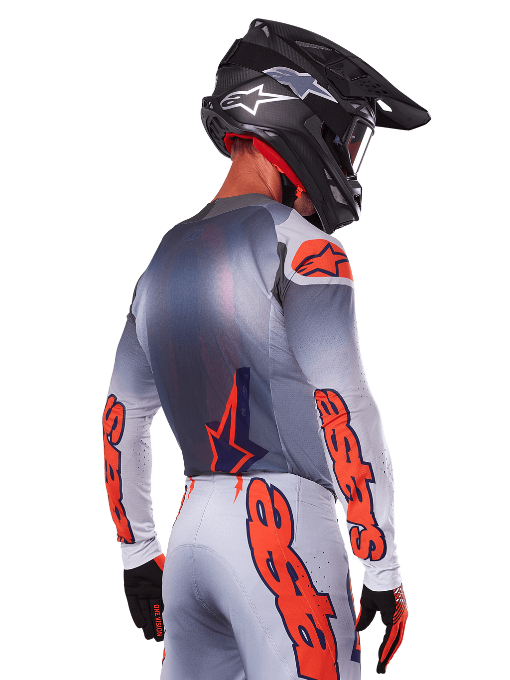 Pilota di motocross visto da dietro con maglia Alpinestars 2025 Supertech Lipan in Grigio Arancione Fluo, con vistosi loghi arancioni sulle maniche e sulla schiena, abbinata a pantaloni coordinati e casco nero, abbigliamento da gara professionale per prestazioni fuoristrada.