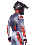 Pilota di motocross visto da dietro con maglia Alpinestars 2025 Supertech Lipan in Grigio Arancione Fluo, con vistosi loghi arancioni sulle maniche e sulla schiena, abbinata a pantaloni coordinati e casco nero, abbigliamento da gara professionale per prestazioni fuoristrada.