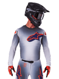 Alpinestars 2025 Supertech Lipan Jersey, maglia da motocross, grigio con accenti arancioni e blu navy, maglia tecnica a maniche lunghe con dettagli di ventilazione traforati, indossata con casco nero e guanti rossi, design racing elegante