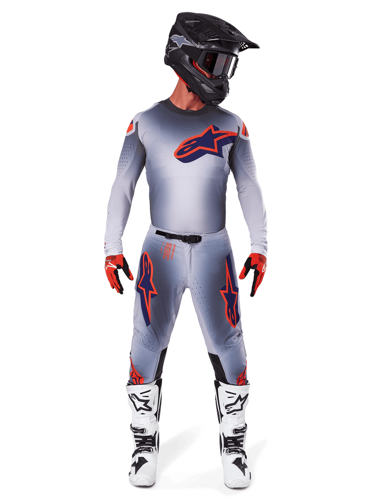 Pilota di motocross che indossa il Set Gear Supertech Lipan 2025 in Grigio Arancione Fluo, con maglia grigia con accenti arancioni e logo Alpinestars blu navy, pantaloni grigi coordinati con grandi loghi sulle cosce, casco nero opaco, stivali bianchi e neri e guanti rossi e neri, abbigliamento completo da gara di livello professionale.