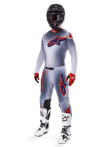 Motocross rider wearing the Alpinestars 2025 Supertech Lipan Jersey in Gray and Orange Fluo, matching gray pants with orange accents, black helmet, white and black boots, and orange and black gloves, professional gear set for off-road racing