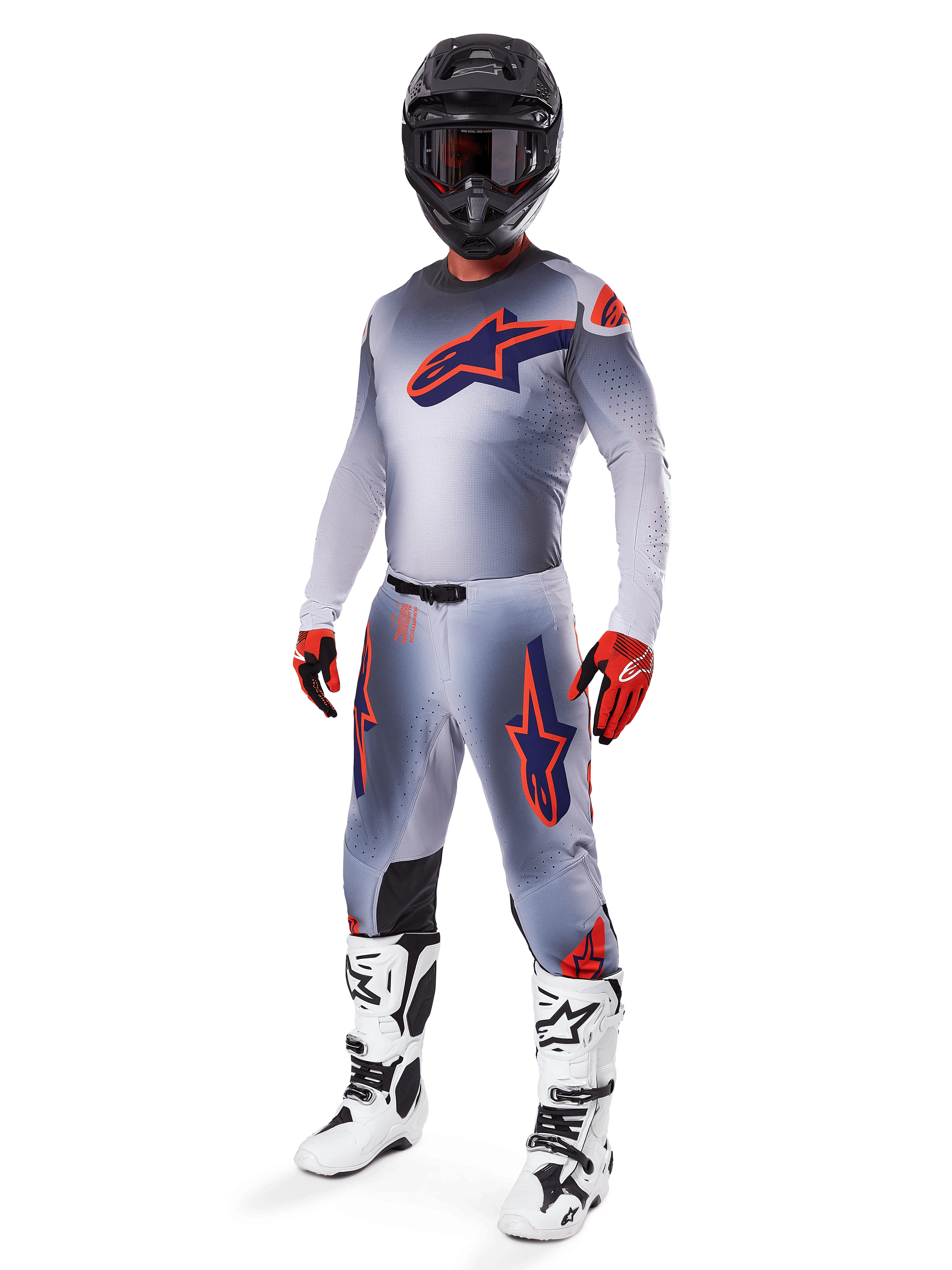Pilota di motocross con maglia Alpinestars Supertech Lipan 2025 in grigio e arancione fluo, pantaloni grigi coordinati con accenti arancioni, casco nero, stivali bianchi e neri e guanti arancioni e neri, set professionale per gare fuoristrada