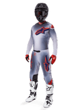Alpinestars 2025 Supertech Lipan Gear Set, abbigliamento da motocross, grigio con grafiche a stella arancione fluo e blu navy, indossato con casco nero, guanti rossi e neri e stivali bianchi e neri, completo professionale da fuoristrada con design ventilato