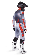 Pilota di motocross visto da dietro che indossa il set 2025 Supertech Lipan, maglia grigia e arancione fluo con pantaloni coordinati, marchio Alpinestars arancione su maniche e gambe, casco nero, stivali da motocross bianchi e neri, completo professionale coordinato da gara off-road.
