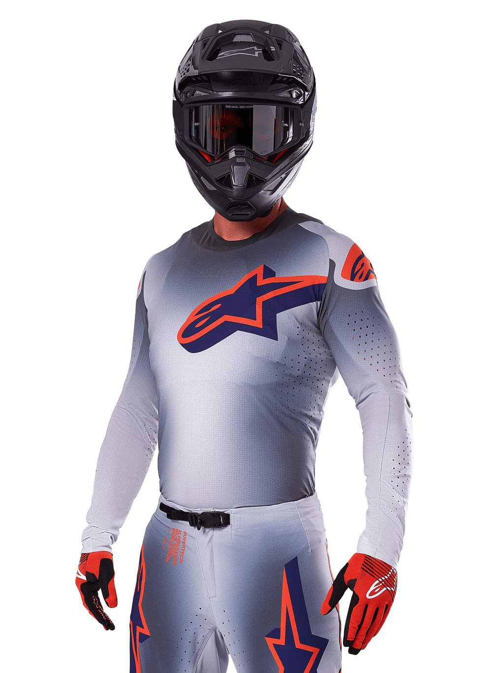 Pilota di motocross con Set Gear Alpinestars 2025 Supertech Lipan, maglia e pantaloni grigi con accenti blu navy e arancioni, casco nero opaco con occhiali e guanti rossi e neri, abbigliamento tecnico per corse fuoristrada