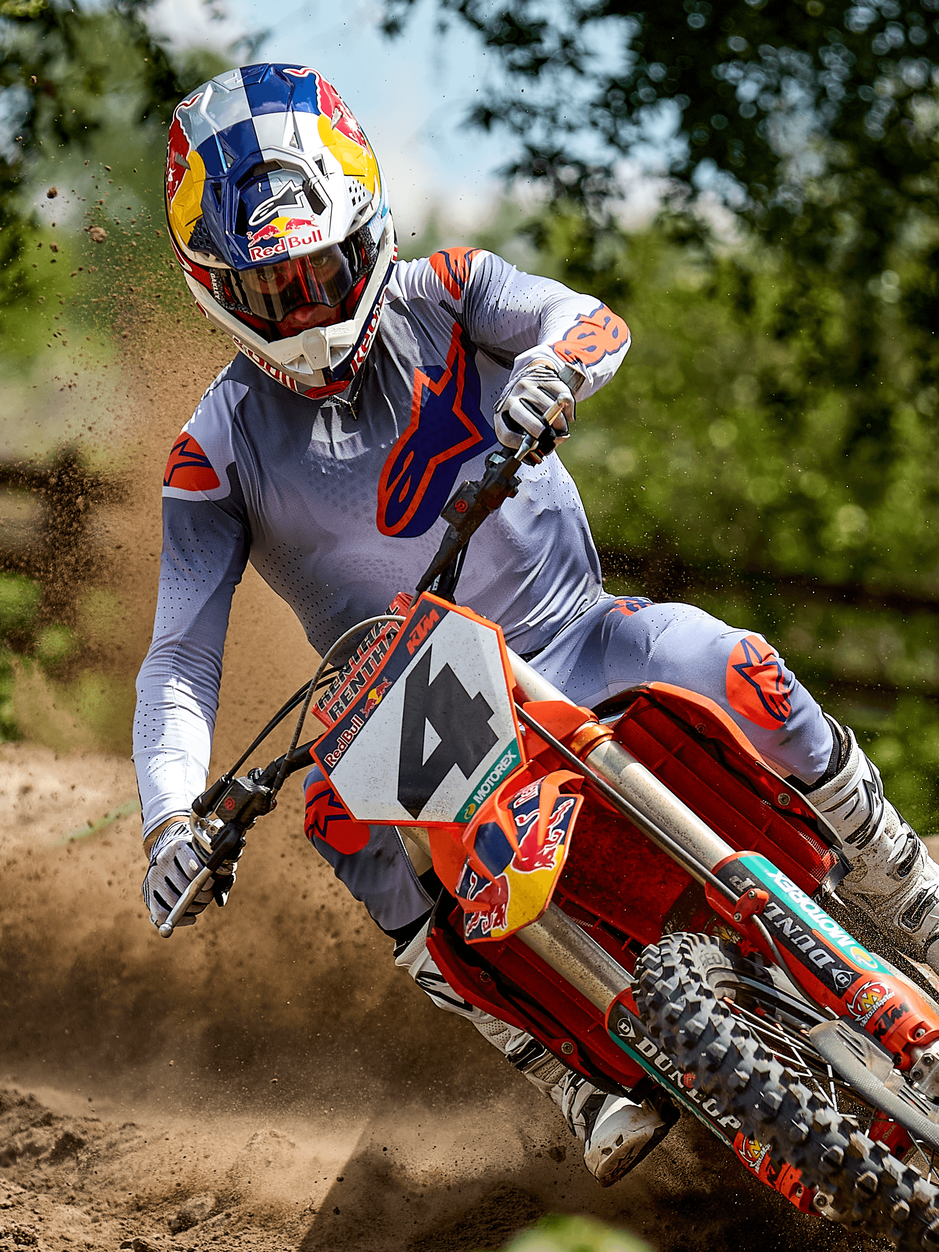 Pilota di motocross in azione con il set completo Alpinestars Supertech Lipan 2025 in grigio e arancione fluo, maglia e pantaloni grigio chiaro con vivaci loghi Astars arancioni, stivali bianchi e casco Red Bull su moto KTM arancione.