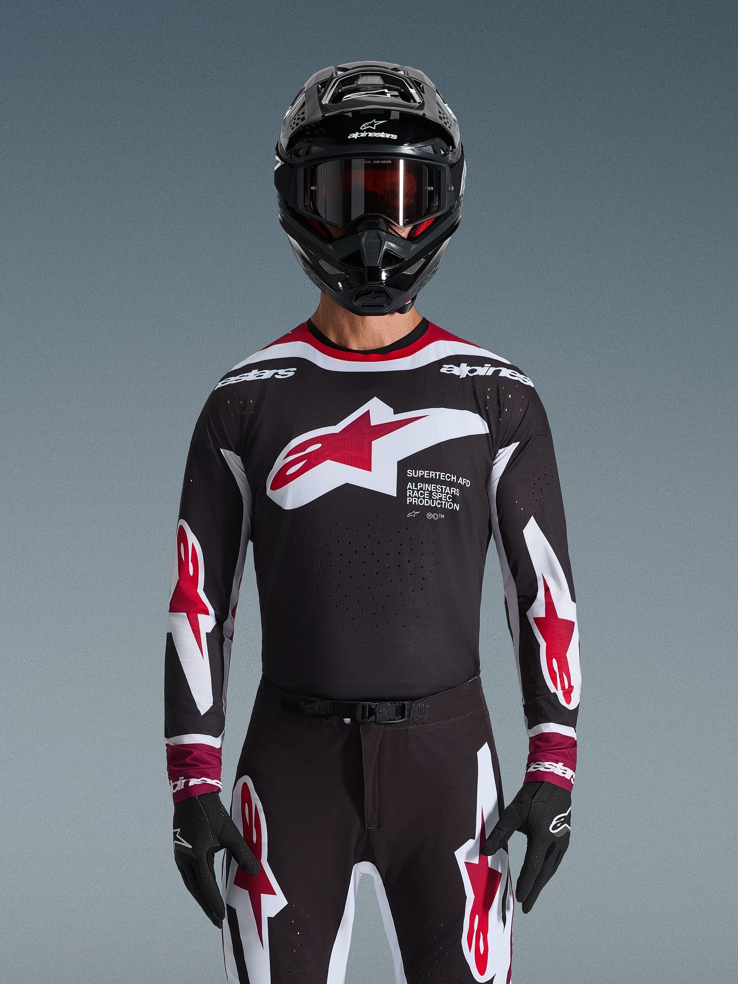 Alpinestars 2026 Supertech AFD Vista Jersey, maglia da motocross in nero, rosso e bianco, mostrata su un pilota con casco nero, occhiali e guanti, con un grande logo sul petto e marchio 'SUPERTECH AFD', abbigliamento da gara professionale per prestazioni fuoristrada