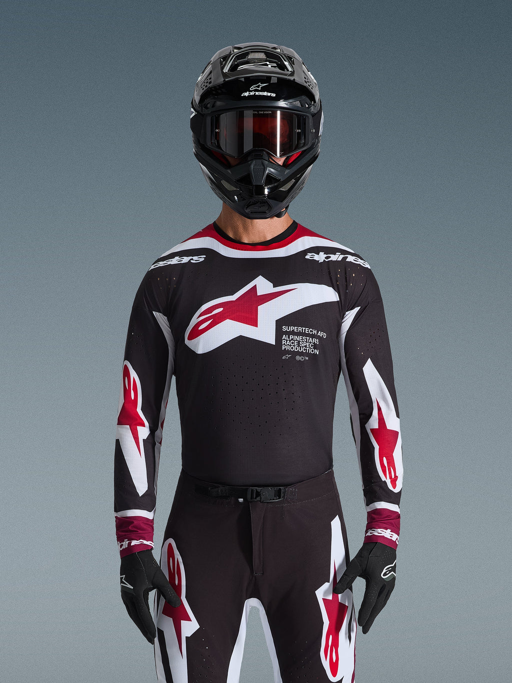 Alpinestars Completo Supertech AFD Vista 2026, completo da motocross, maglia nera con loghi rossi e bianchi e marchio 'Supertech AFD', pantaloni neri coordinati con accenti rossi, casco nero con occhiali rossi, outfit da gara professionale