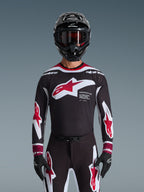 Alpinestars Completo Supertech AFD Vista 2026, completo da motocross, maglia nera con loghi rossi e bianchi e marchio 'Supertech AFD', pantaloni neri coordinati con accenti rossi, casco nero con occhiali rossi, outfit da gara professionale