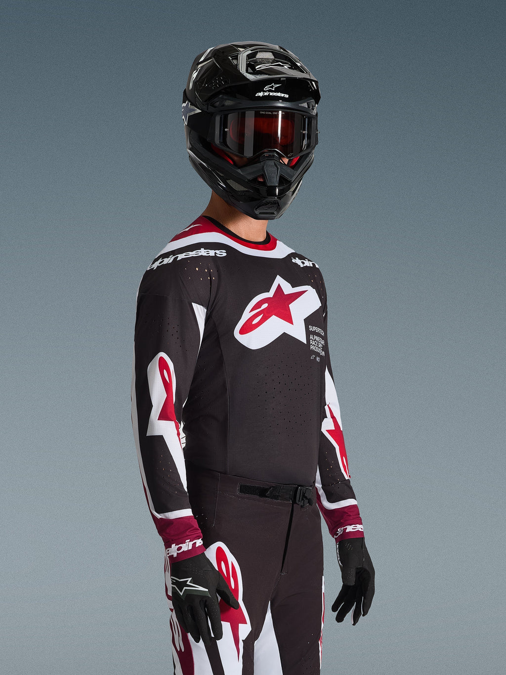 Alpinestars 2026 Supertech AFD Vista Jersey, pilota di motocross con abbigliamento da gara completo, maglia nera con accenti rossi e bianchi, grande logo sul petto, traforature laser, indossata con pantaloni coordinati, casco nero e maschera rossa, completo coordinato per gare fuoristrada
